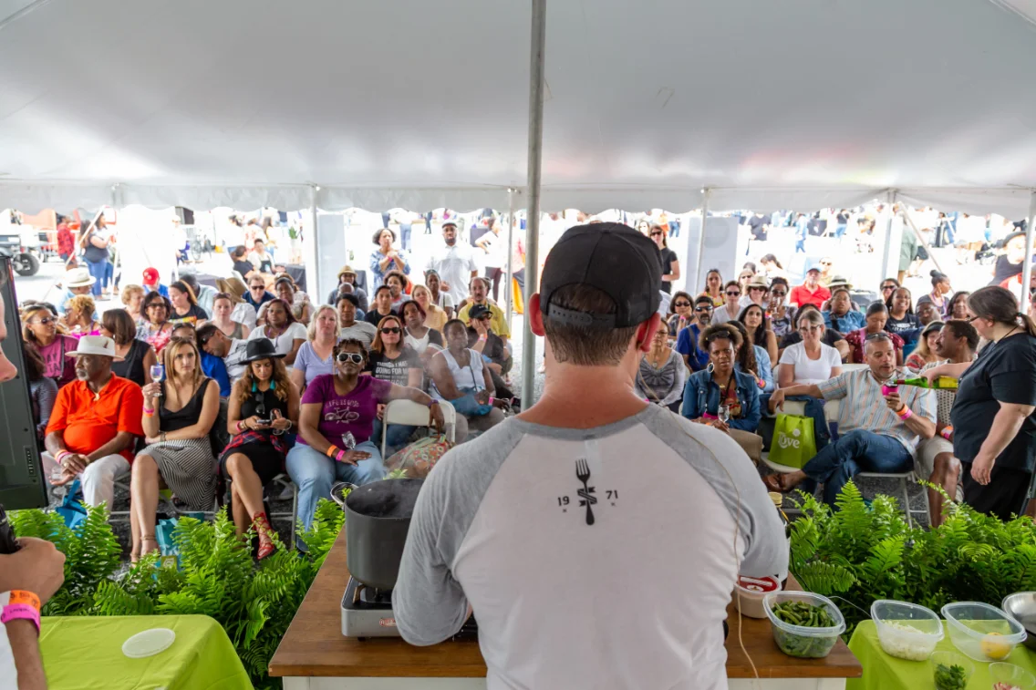 A seated crowd under a tent watching a live cooking demonstration