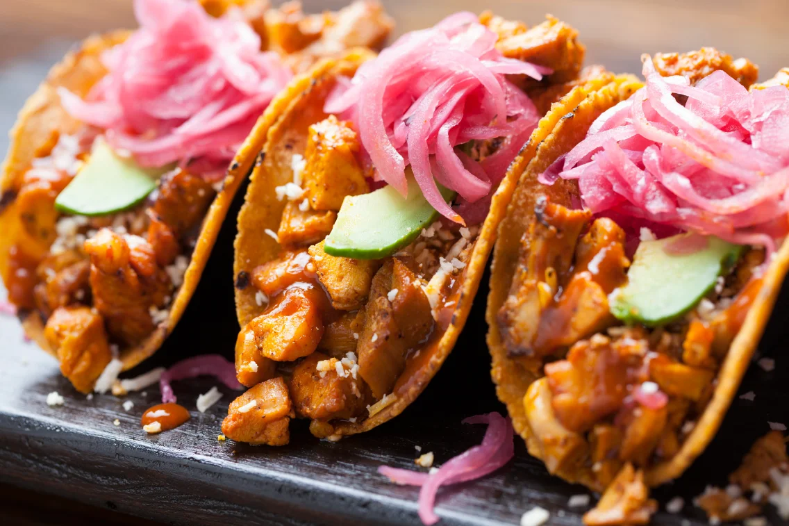 Close-up of three tacos topped with pickled onion