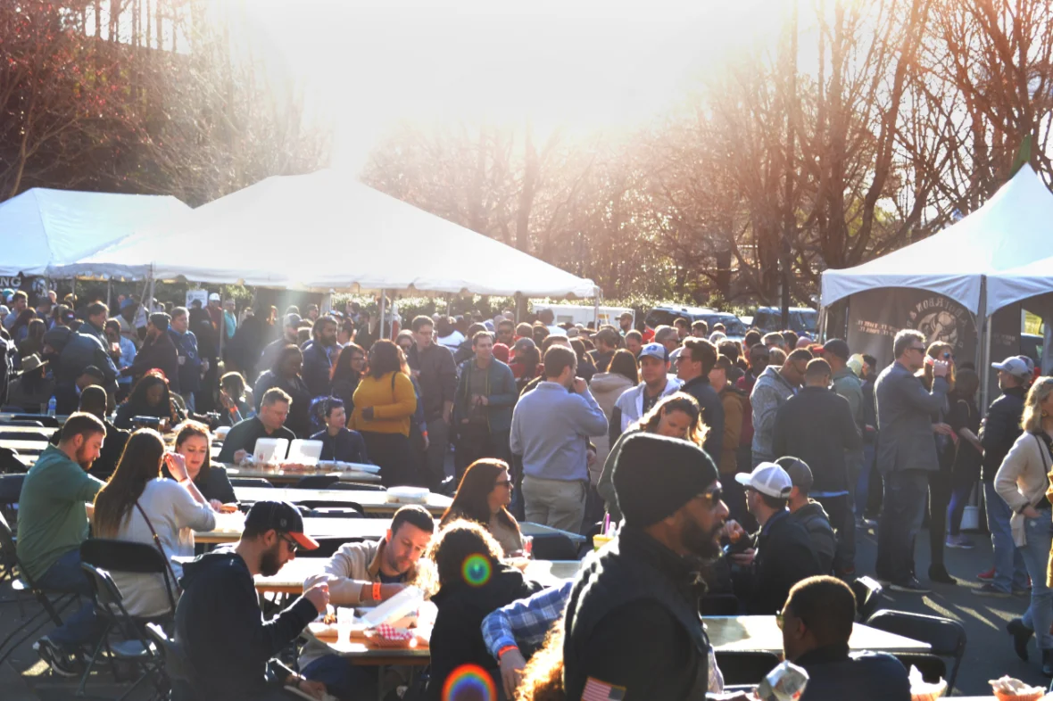 A busy festival crowd at picnic tables under open-sided tents