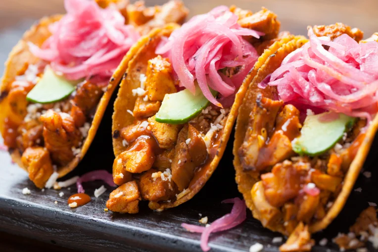 Close-up of three tacos topped with pickled onion