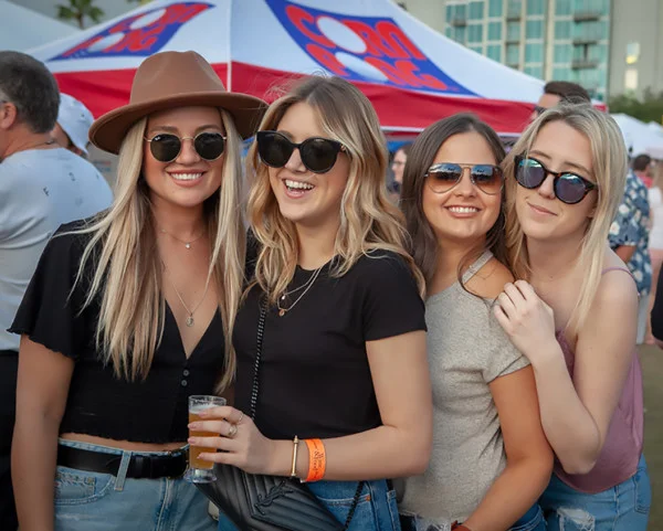 Four guests posing together with drinks at an outdoor festival