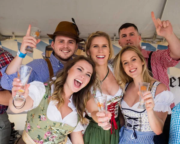 Guests in Oktoberfest dress raising glasses together under a festival tent